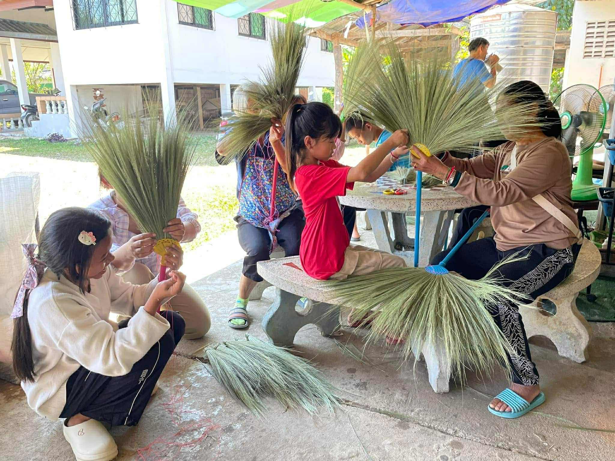 "Together in Craft: Children, youth, and families join forces to sew and attach broom handles, crafting quality products while building community bonds."