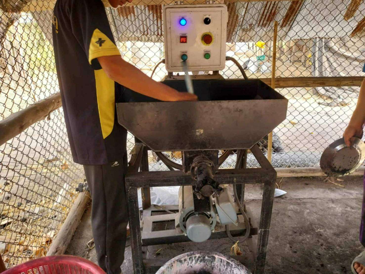 Children help prepare the machine to press the charcoal, showcasing their active participation and learning in sustainable energy generation