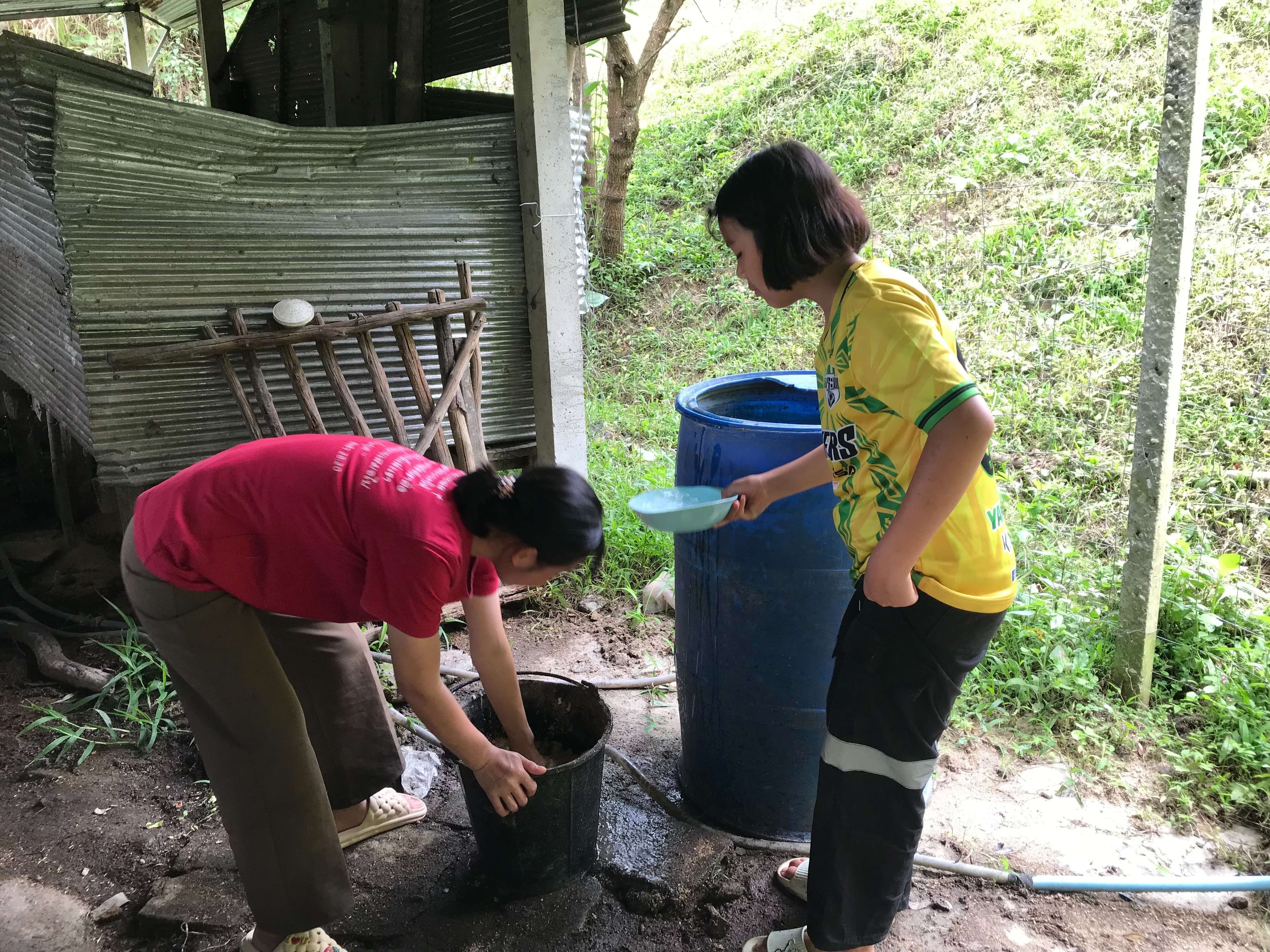 Children mixing feed to prepare pig food.