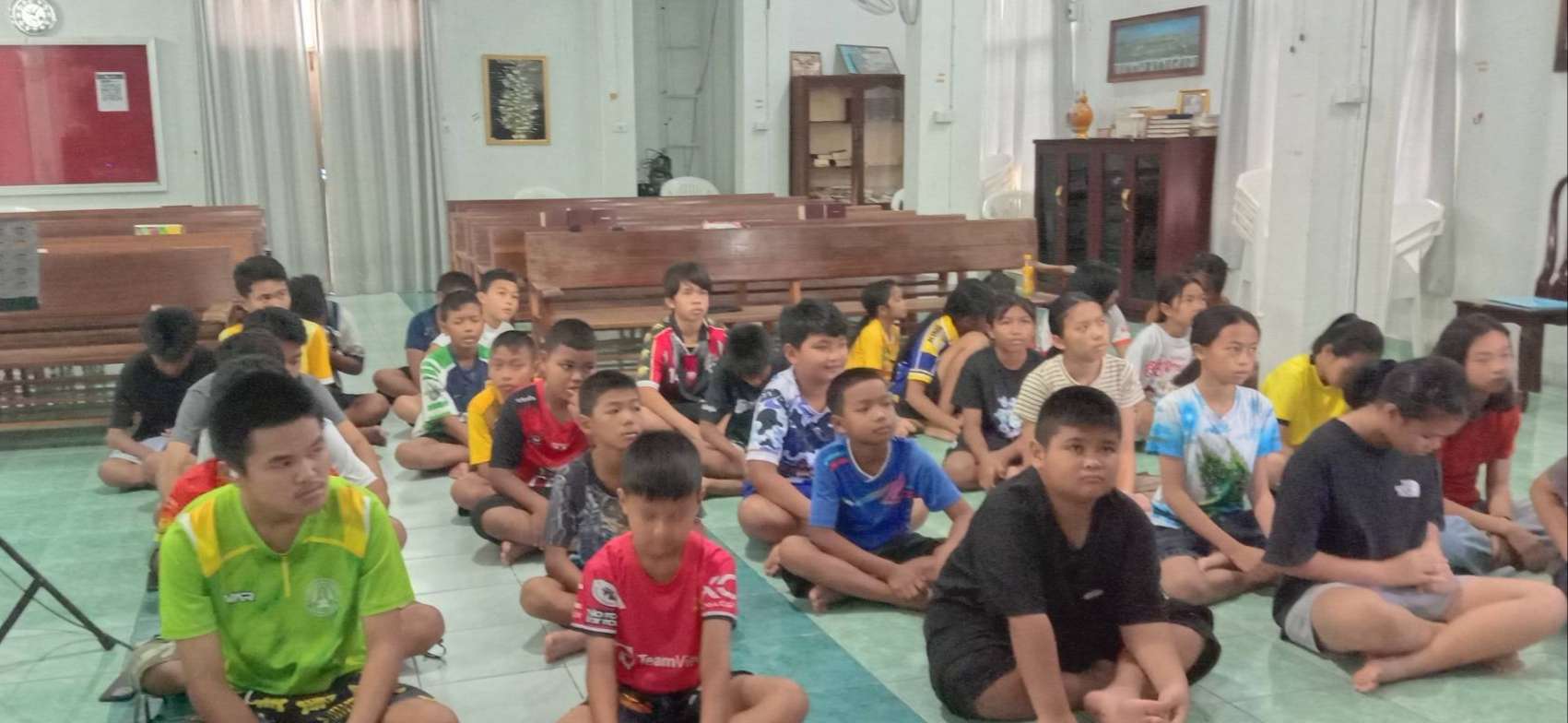 The children are sitting and listening to the teacher.