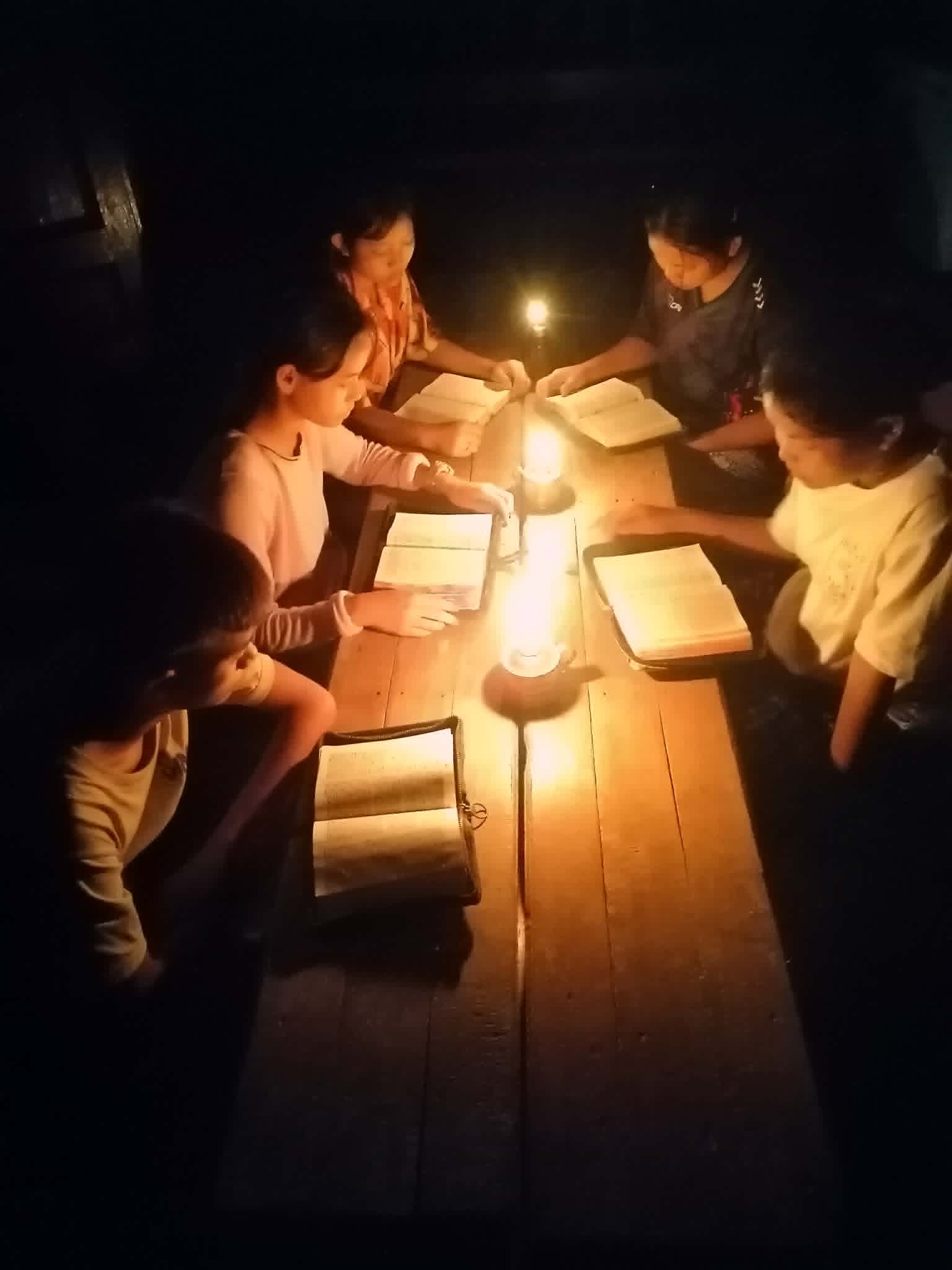 Children read the Bible under candlelight.