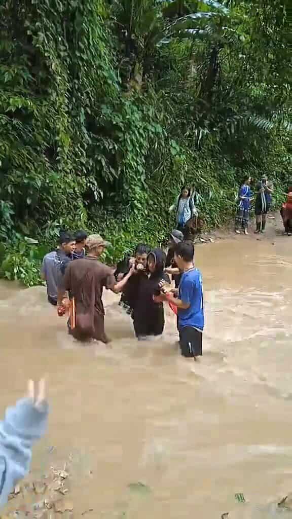 A group of people wading through knee-deep muddy water during the rainny season