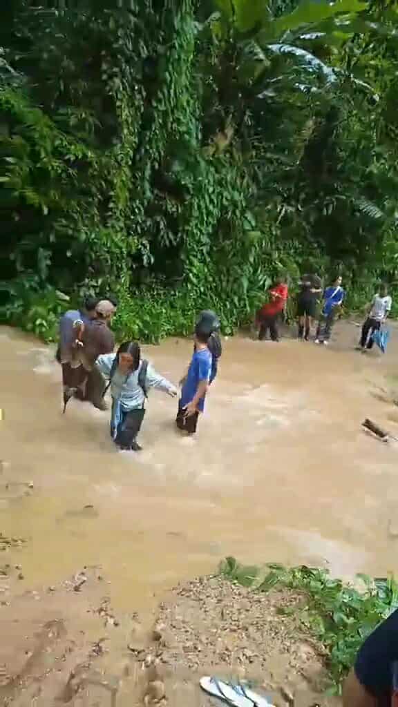 "Braving the elements: A group of children wade through knee-deep water in muddy conditions on their way to school."