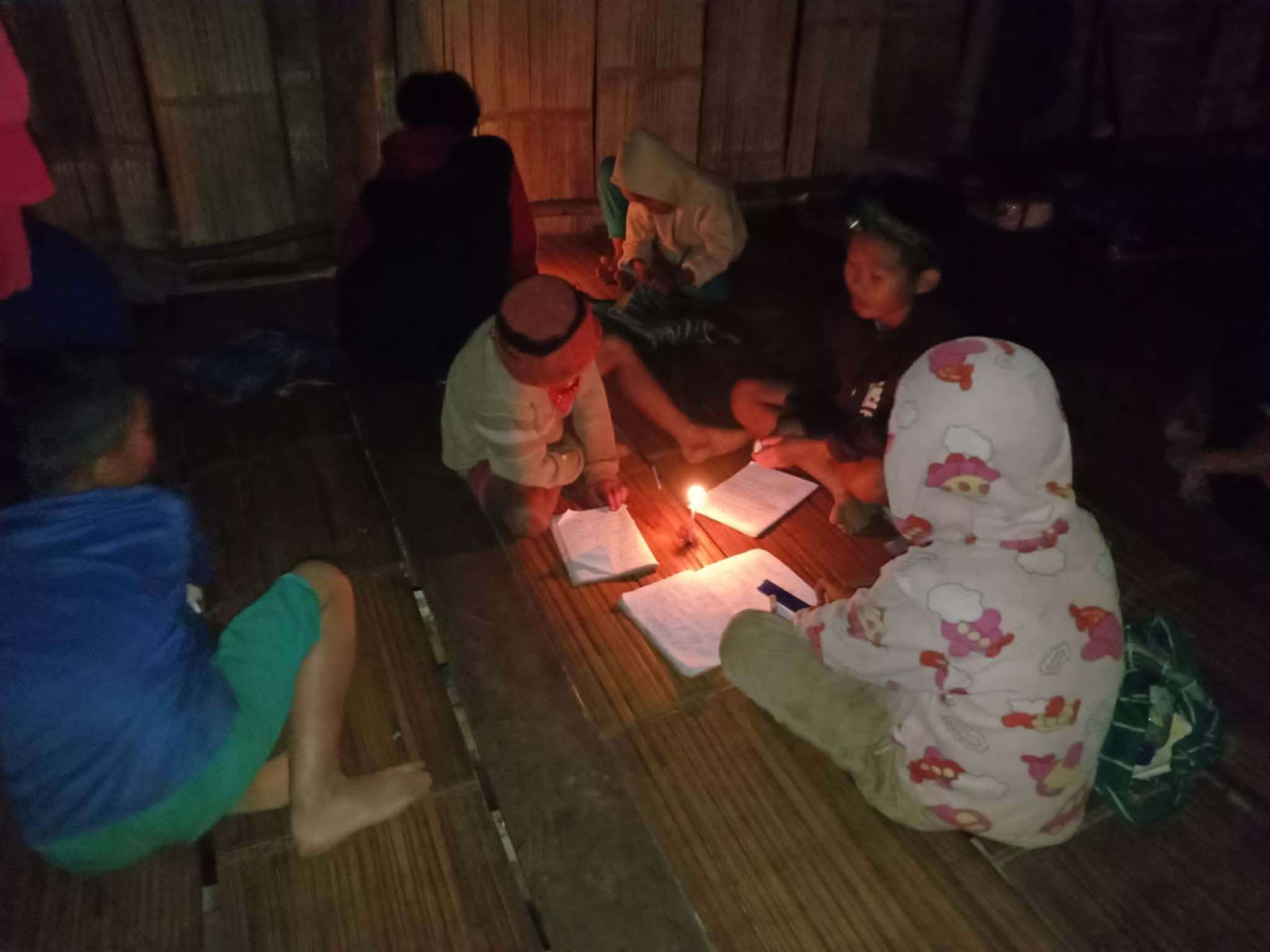 Nighttime Study: Children unite with torchlight to tackle their homework, brightening their future together.