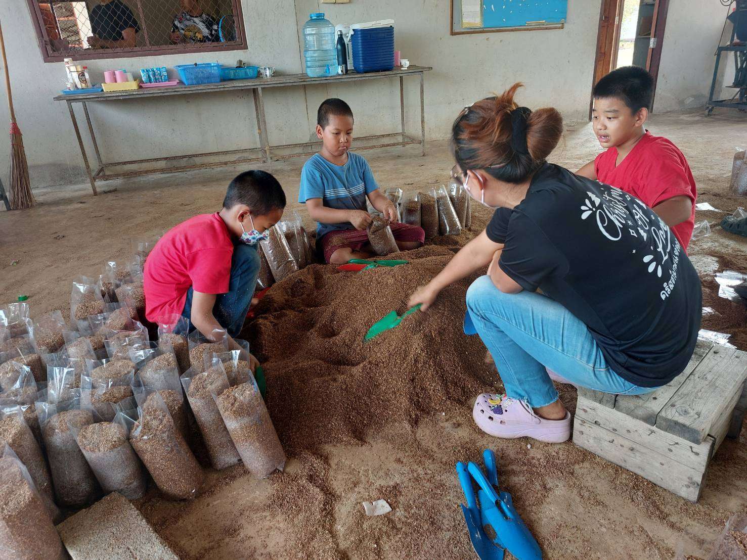 Teachers and children are helping to scoop sawdust into bags.