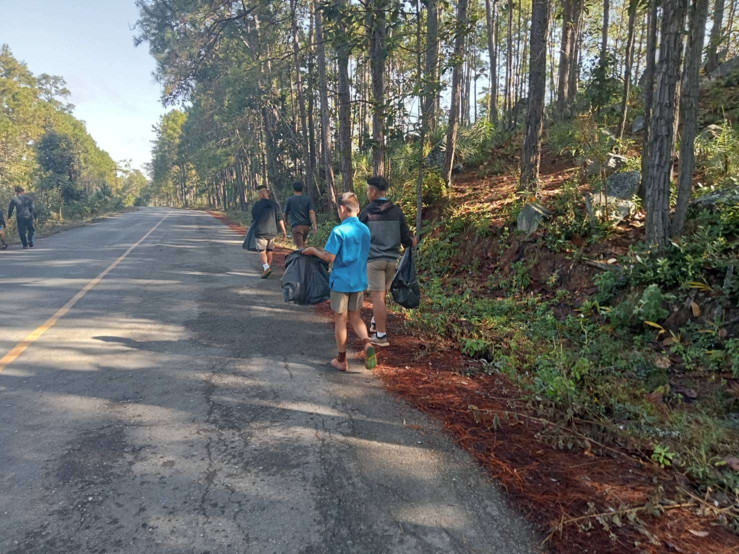 Young children collect garbage on the side of the road.