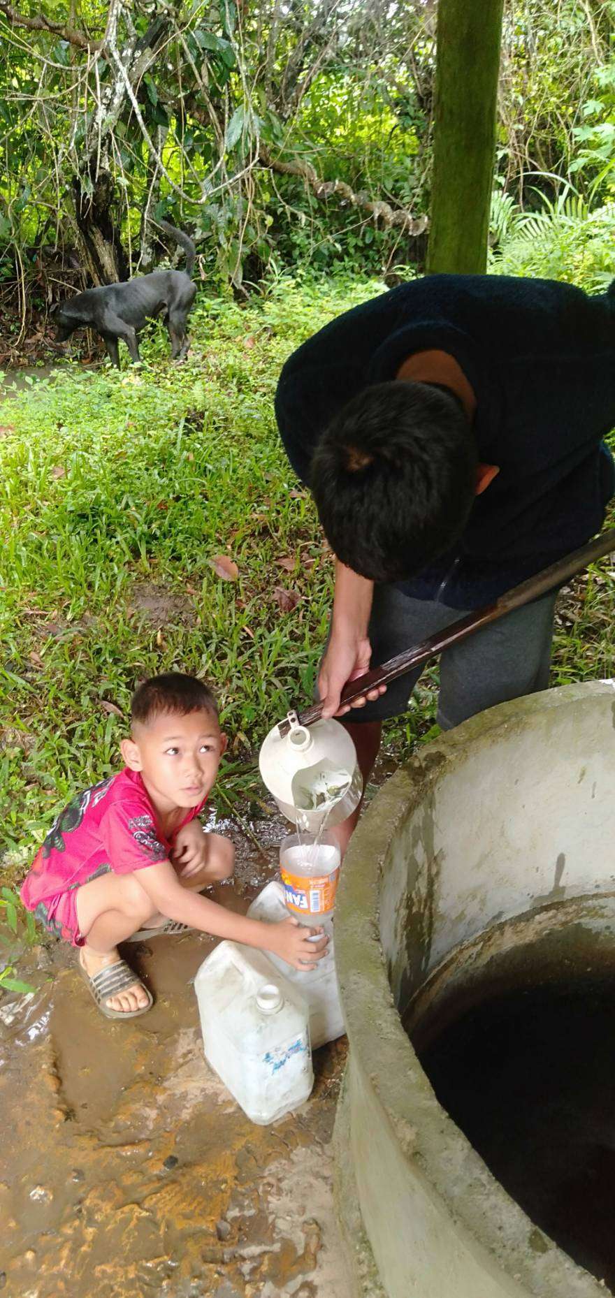 Children and his parent are scooping water from a well.