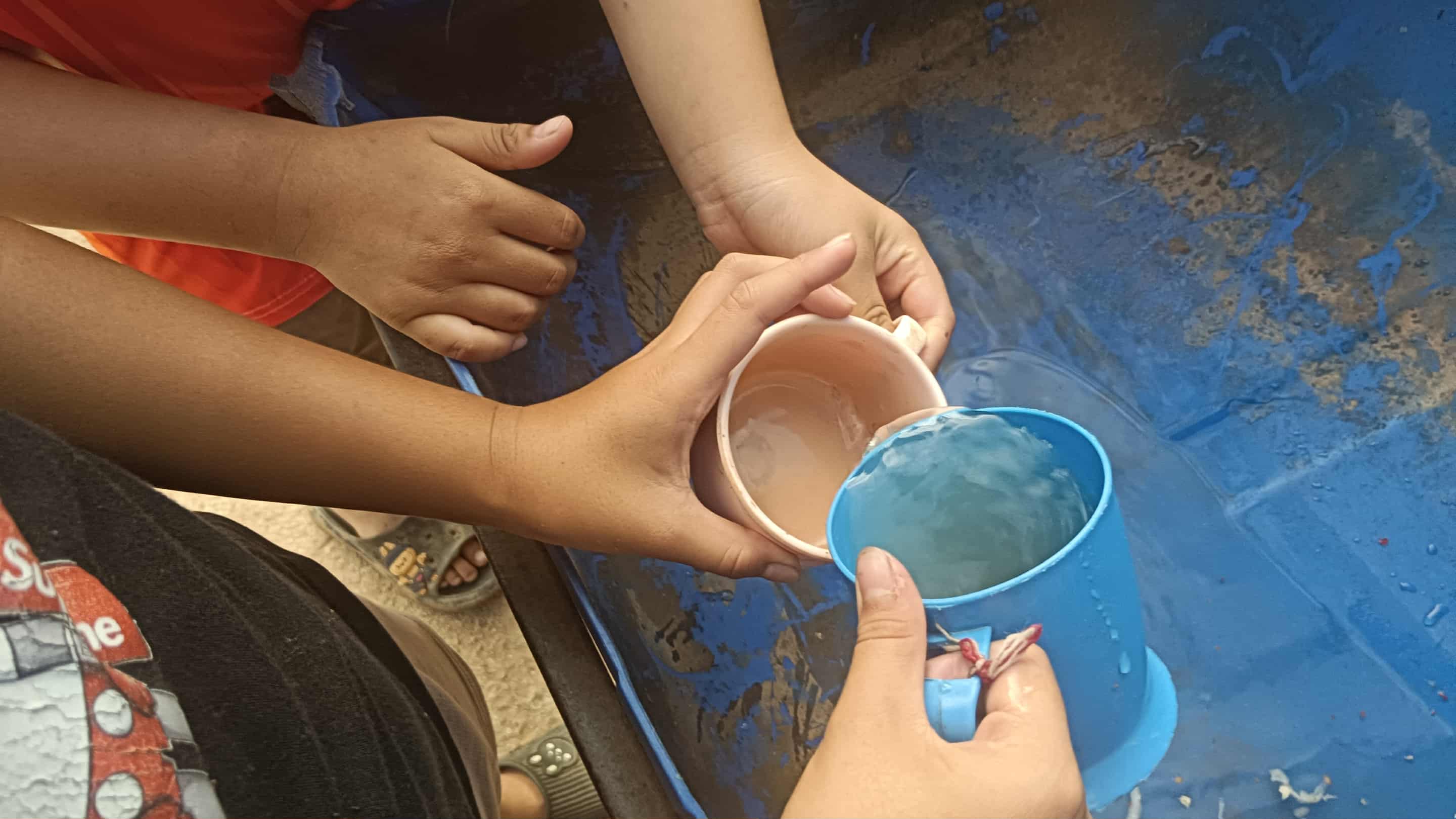 Children scoop up cloudy water from a glass, hoping to drink clean water for their health.